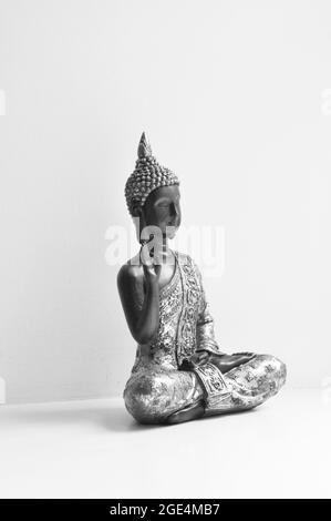 Buddha statue set to the right of the image against a white background. Image is in black and white Stock Photo