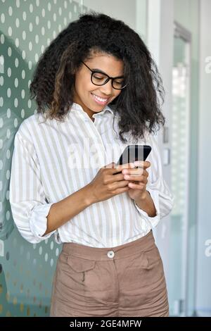 Smiling young African American business woman using phone standing in office. Stock Photo