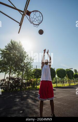 Wide angle view of african american player throwing ball in basketball hoop outdoors Stock Photo