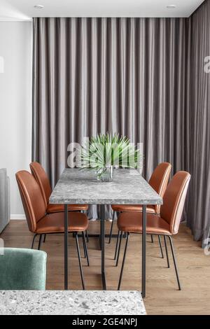 Grey Dining marble stone table with four rust leather chairs and grey curtains in Scandinavian minimalist dining room interior Stock Photo