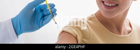 partial view of doctor in latex glove vaccinating smiling woman, banner Stock Photo