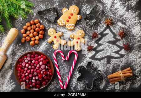 Christmas food. Ingredients for Christmas baking:  fir tree made from flour, kitchen utensils, frozen cranberries and gingerbread cookies on a dark ta Stock Photo