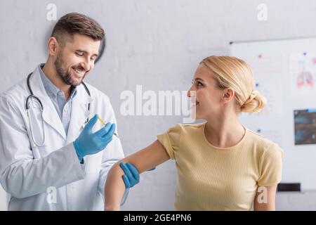 positive doctor in latex gloves vaccinating happy woman in clinic Stock Photo