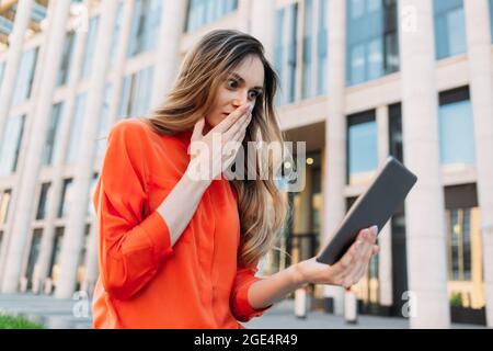 Caucasian woman holding a tablet in her hands and looking shocked. Stock Photo