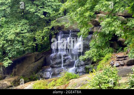 A picturesque waterfall flows on a small river among green trees in Sofievsky Park in autumn, summer. Uman, Ukraine, long exposure Stock Photo