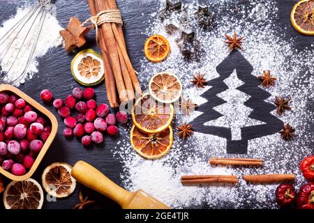 Christmas cooking: fir tree made from flour on a dark table, ingredients for baking, frozen cranberry and dried fruits on dark background, top view Stock Photo