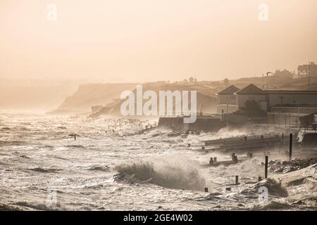 Ferocious waves crash onto the beach at Milford-on-Sea in Hampshire in the summertime with distant cliffs in sunlight. Stock Photo