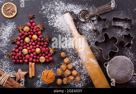 Christmas food. Ingredients for cooking Christmas baking: fir tree made from dried cranberries with nuts, kitchen utensils and dried fruits on a dark Stock Photo