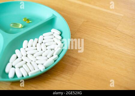 Green plate with dividers filled with pills and capsules. Biohacking movement. Wellbeing concept. Modern medicine with antibiotics. Stock Photo