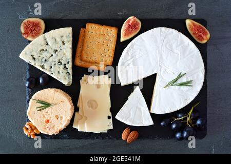 Cheese board with a selection of cheeses, crackers, figs and nuts on slate serving board. Above view on a dark background. Stock Photo