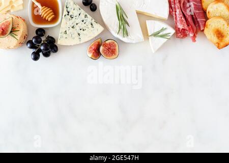 Assorted cheeses and meat appetizers. Top border, overhead view on a white marble background with copy space. Stock Photo