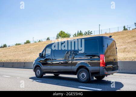Compact industrial small size black mini van with cargo compartment for local deliveries and small business needs running on the wide multiline highwa Stock Photo