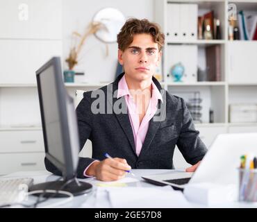 Focused attractive young man working with laptop and documents Stock Photo