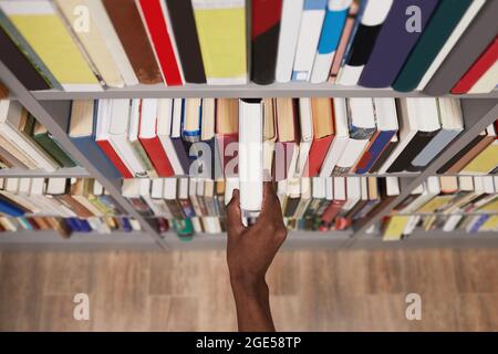 Top view close up of male hand taking book off shelf in library, copy space Stock Photo