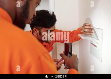 Serious professional electricians in orange uniform installing Watt hour meter in apartment on customer Stock Photo