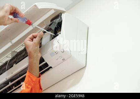 Hands of technician using screwdriver when installing air conditioner in bedroom of customer Stock Photo