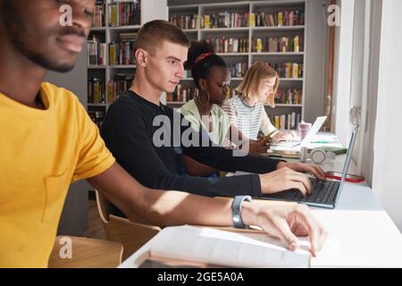 Side view at diverse group of students sitting in row while studying in school library, copy space Stock Photo