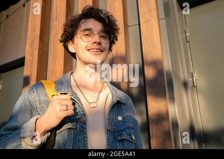 Cheerful guy with backpack looking at you with smile while standing outdoor Stock Photo