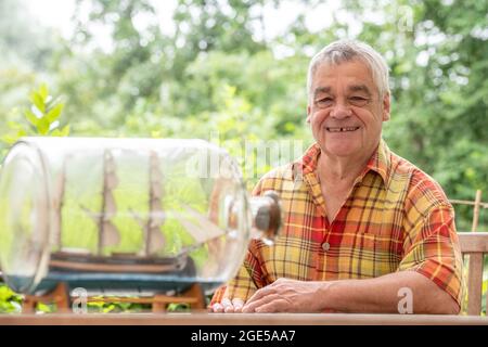 Bochum, Germany. 28th July, 2021. Jürgen Landmann, owner of the Ship in a Bottle Museum, sits in his garden in Bochum. Landmann's father opened the museum in 1971. After his death, his son took over the exhibition, which is seen by around 20,000 visitors every year. Landmann is now looking for a successor for his museum in the Hotel Janssen in Neuharlingersiel. (to dpa 'Mini-Welten unter Glas: Buddelschiffmuseum sucht neuer Besitzer') Credit: Caroline Seidel/dpa/Alamy Live News Stock Photo