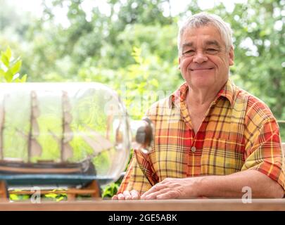 Bochum, Germany. 28th July, 2021. Jürgen Landmann, owner of the Ship in a Bottle Museum, sits in his garden in Bochum. Landmann's father opened the museum in 1971. After his death, his son took over the exhibition, which is seen by around 20,000 visitors every year. Landmann is now looking for a successor for his museum in the Hotel Janssen in Neuharlingersiel. (to dpa 'Mini-Welten unter Glas: Buddelschiffmuseum sucht neuer Besitzer') Credit: Caroline Seidel/dpa/Alamy Live News Stock Photo