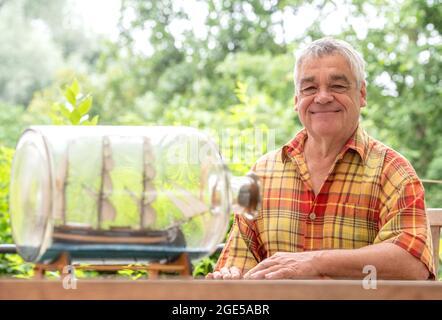 Bochum, Germany. 28th July, 2021. Jürgen Landmann, owner of the Ship in a Bottle Museum, sits in his garden in Bochum. Landmann's father opened the museum in 1971. After his death, his son took over the exhibition, which is seen by around 20,000 visitors every year. Landmann is now looking for a successor for his museum in the Hotel Janssen in Neuharlingersiel. (to dpa 'Mini-Welten unter Glas: Buddelschiffmuseum sucht neuer Besitzer') Credit: Caroline Seidel/dpa/Alamy Live News Stock Photo