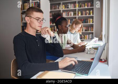 Side view portrait of three students sitting in row at desk while studying in school library, copy space Stock Photo