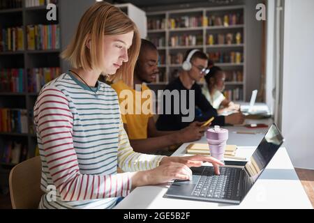 Side view portrait of young woman studying with group of students in school library, copy space Stock Photo