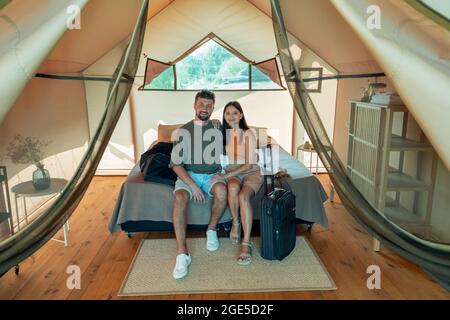 Young affectionate couple sitting on double bed inside glamping house while on travel Stock Photo