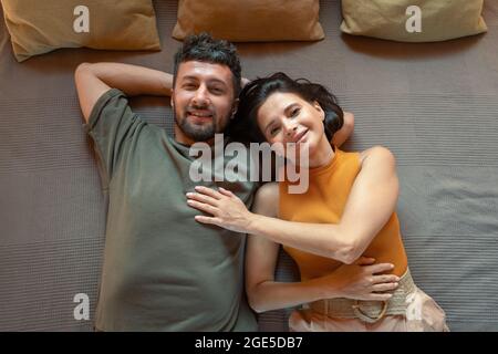 Cheerful and affectionate young couple lying on bed in front of camera Stock Photo