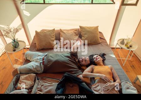 Happy idyllic couple relaxing on large bed in glamping house while enjoying summer rest Stock Photo