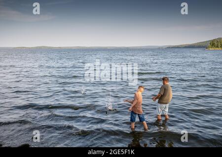 Young man and teenage boy standing in the lake and throwing stones into water on summer day Stock Photo