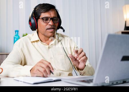 Middled aged Businessman with headphones attending online and making notes glass from office - concept of never stop learning and business training Stock Photo