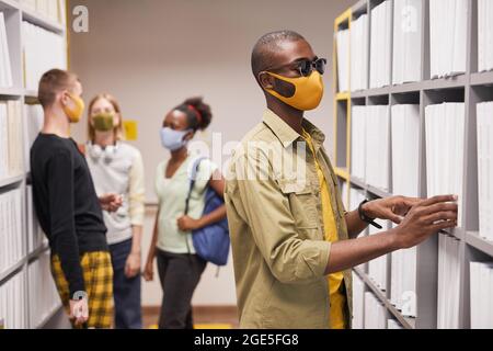 Portrait of blind African-American man wearing mask while choosing book in library Stock Photo