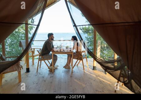 Young romantic couple holding by hands while enjoying breakfast on terrace by seaside Stock Photo