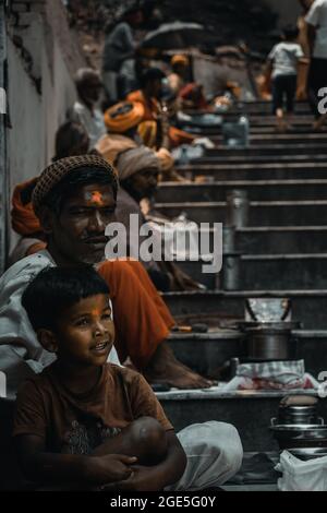 Street photograph of a poor child beggar sitting on the stairs among other beggars in the city of Dehradun, Uttarakhand, India Stock Photo