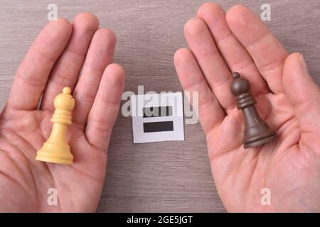 Multiracial equality concept with hands with different color chess pieces in each hand on wooden table holding sign with equal sign. Top view. Stock Photo