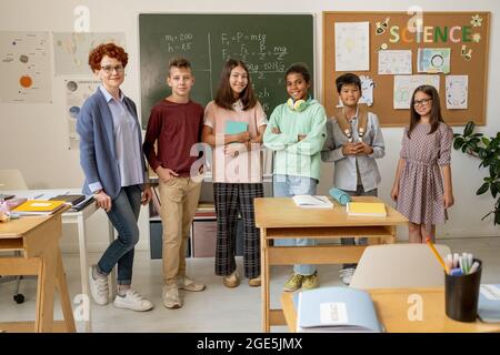 Young successful teacher and group of secondary school students standing against blackboards Stock Photo