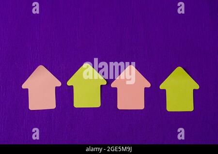 Paper sticky notes in shape of arrow on lilac background. Pink and yellow arrows in a row. Top view Stock Photo