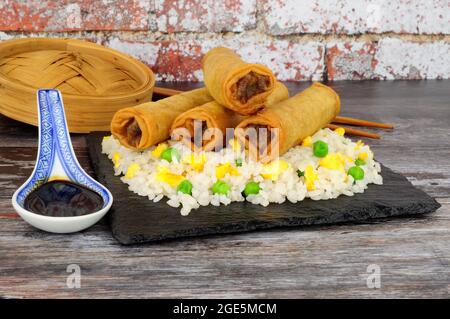 Chinese crispy duck and vegetable filled spring rolls with egg rice on a slate serving board Stock Photo