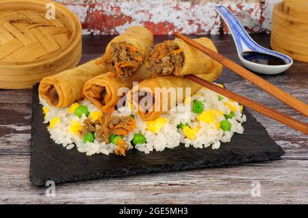 Chinese crispy duck and vegetable filled spring rolls with egg rice on a slate serving board Stock Photo