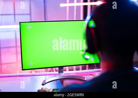 Shoulder shot of professional video gamer playing video game on Agreen screen computer monitor - concept of esports tournment on neon light background Stock Photo