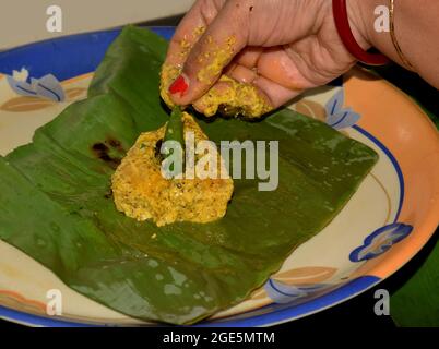 Bengali women preparing Ilish paturi dish where fish is smeared with mustard oil and poppy seeds before covering it with banana leaf and then kept it Stock Photo