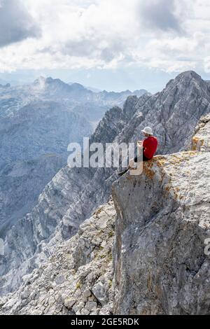 Hiker with helmet sitting on rocks, Watzmann middle peak, hiking trail to the Watzmann, Watzmann crossing, Berchtesgaden, Bavaria, Germany Stock Photo