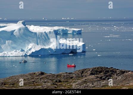 Red fishing boat in a bay with huge icebergs, wide bay with icebergs behind it bay with icebergs, Ilulissat, Arctic, North America, Greenland, Denmark Stock Photo