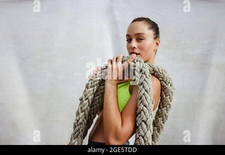 Female athlete holding battle rope. Fit woman with battling rope in looking at camera while exercising. Stock Photo
