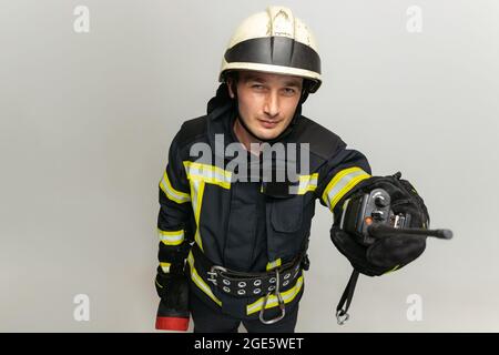 One male firefighter dressed in uniform posing over white studio background. Stock Photo