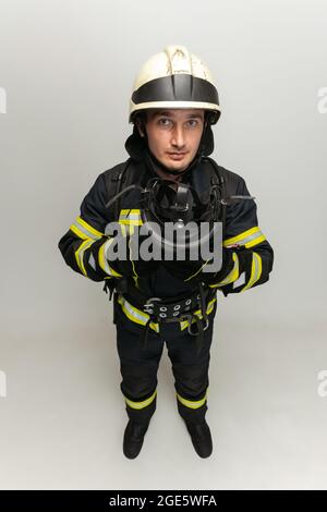 One male firefighter dressed in uniform posing over white studio background. Stock Photo