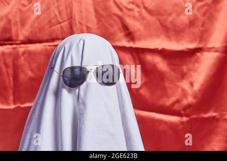 White ghost on orange. Halloween holiday. A young child dressed in a ghost costume for Halloween on orange background. Funny Halloween kid. Little Stock Photo