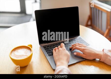 Unrecognizable young woman using laptop with blank screen and typing on keyboard, sitting in the Internet cafe, crop, copy space. Mockup for your desi Stock Photo