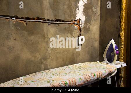 Socket. Iron and ironing board. Repair in the house. Electricity wiring. Socket. Wires. Plastered walls Stock Photo